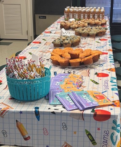 Muffins and juice on long table with table cloth, pencils and flyers